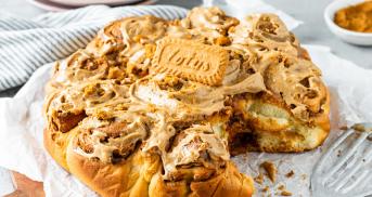 Zimtschnecken aneinander gebacken auf einem Teller, eine fehlt, getoppt mit Frosting und einem Lotus-Keks