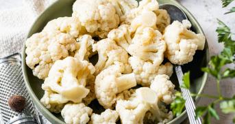 Damfgegarte Blumenkohlröschen in einer Schale auf einem Holzbrett, daneben grobes Salz