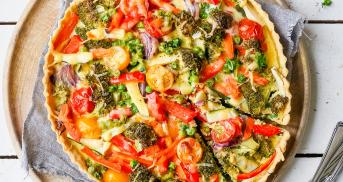 Gemüsequiche angeschnitten mit Tomaten, Paprika, Erbsen, Zucchini und Möhren