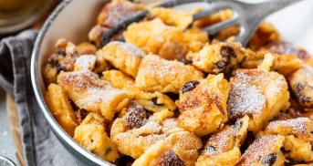 Kaiserschmarrn in einer Pfanne, daneben ein Glas selbstgemachtes Apfelmus