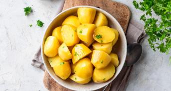 Damfgegarte Kartoffeln in einem tiefen Teller, dekoriert mit frischer Petersilie auf einem Tisch, daneben Salz und Pfeffer