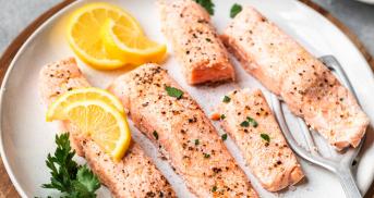 Dampfgegarte Lachsfilets auf einem Teller dekoriert mit Zitronenspalten und frischen Petersilie