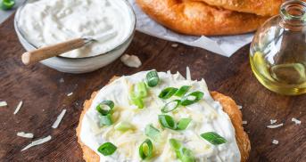 Langos mit Knoblauchcreme, Käse und Frühlingszwiebeln auf einem Holzuntergrund.