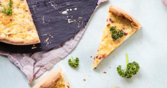 Ein angeschnittener Schwäbischer Zwiebelkuchen steht auf einer Kuchenplatte. Drei Tortenstücke sind herausgeschnitten.