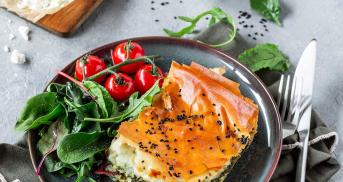 Ein Stück Spanakopita auf einem Teller mit Salat und Tomaten.