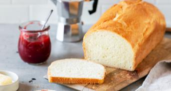 Toastbrot angeschnitten auf einem Brettchen, daneben Butter und Marmelade