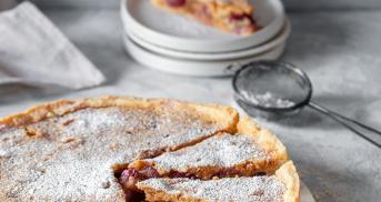 Traubenkuchen mit Mandelguss angeschnitten auf einer Kuchenplatte.
