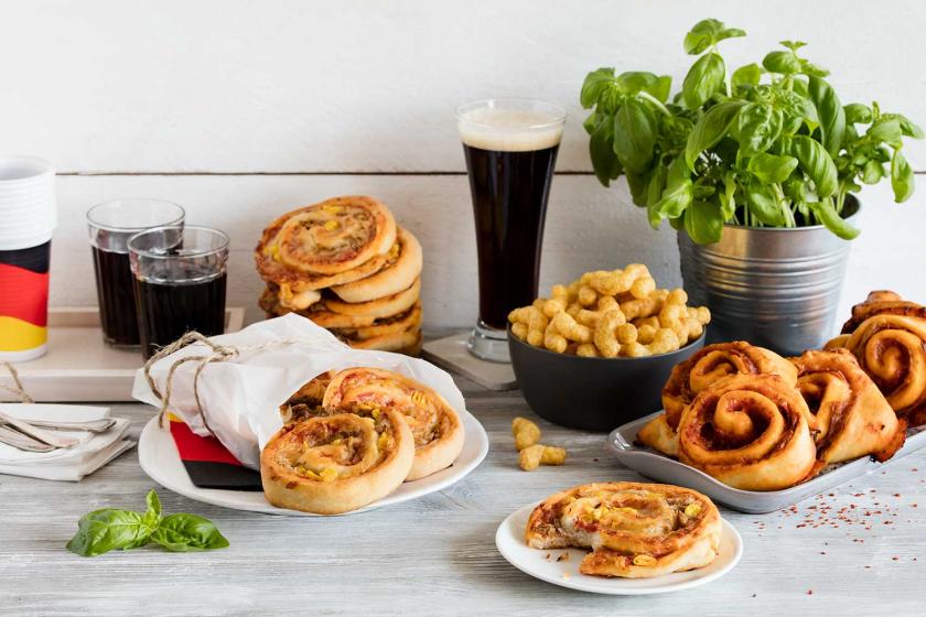Verschiedene Pizzaschnecken sind auf Tellern angerichtet und stehen auf einem Tisch mit Chips und Bier.