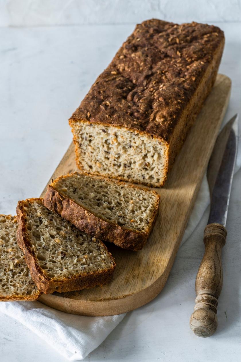 Dinkelbrot aufgeschnitten auf einem Brett und eine Scheibe mit Butter bestrichen.