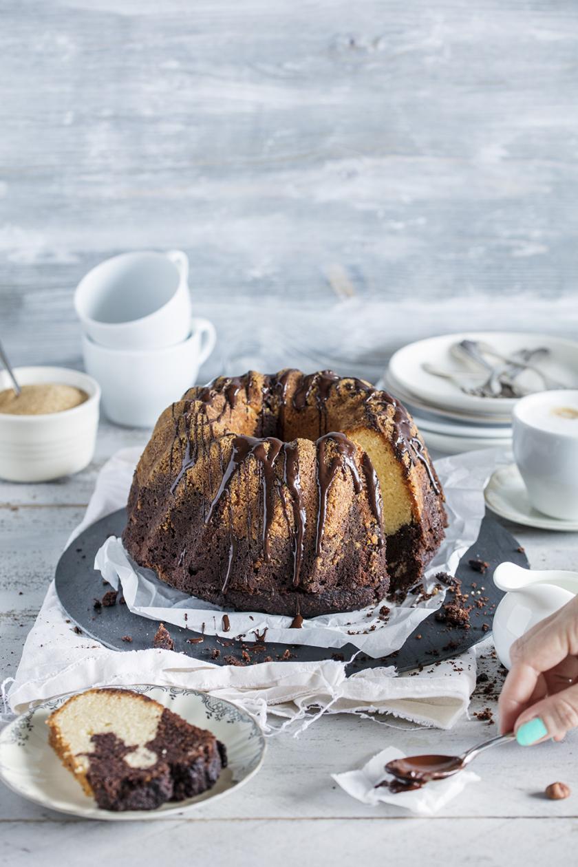 Ein angeschnittener Low Carb Marmorkuchen steht auf einem gedeckten Tisch. Ein Stück liegt auf einem Kuchenteller daneben.