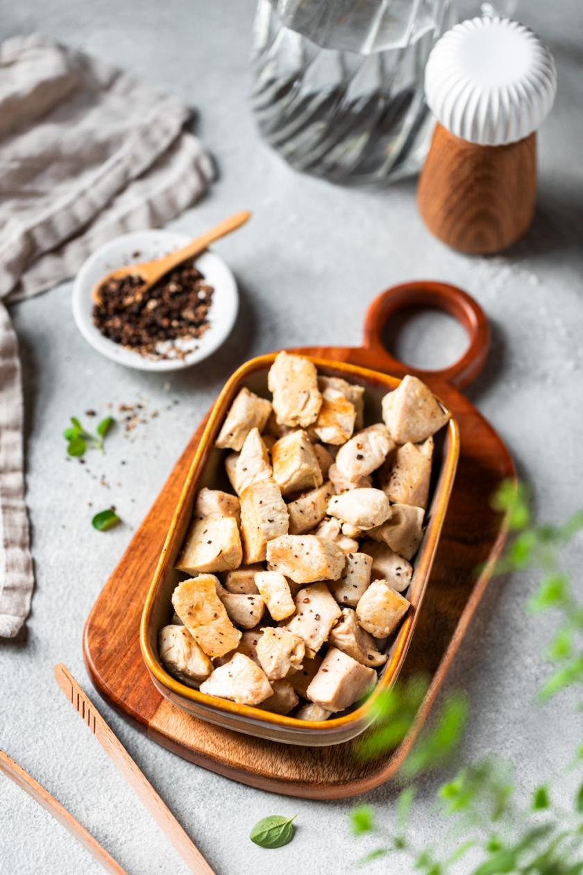 Dampfgegartes Hähnchen in Würfeln in einer Steingutform auf einem Tisch, daneben Gewürze in einer Schale