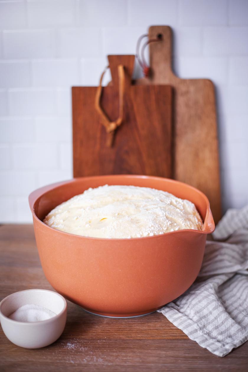 Hefeteig in einer orangenen Schüssel auf Arbeitsfläche.