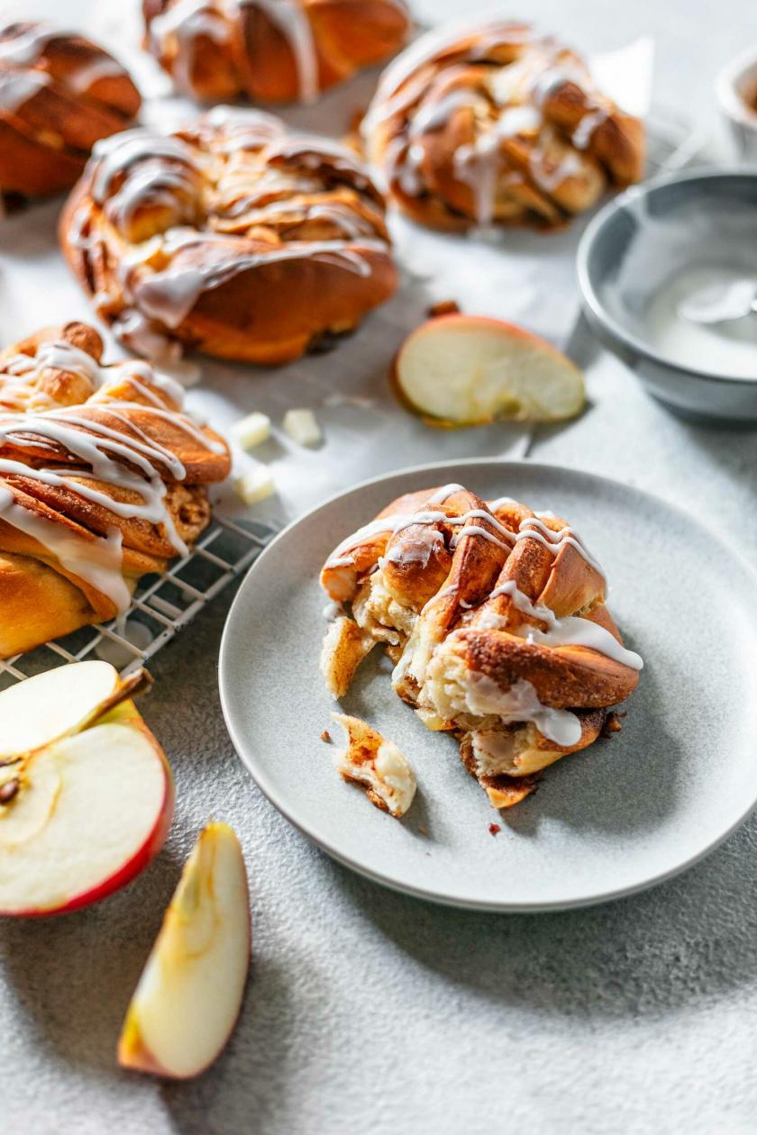 Apfel-Zimt-Knoten auf einem Telle im close up, daneben Apfelspalten auf einem Tisch