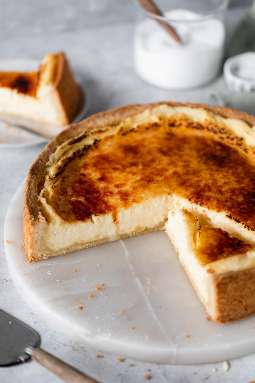 Creme Brulee Kuchen angeschnitten auf einer Kuchenplatte, daneben ein Stück auf einem Kuchenteller