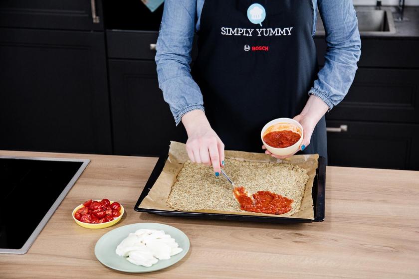 Der Boden der Blumenkohlpizza wird mit Tomatensauce bestrichen.