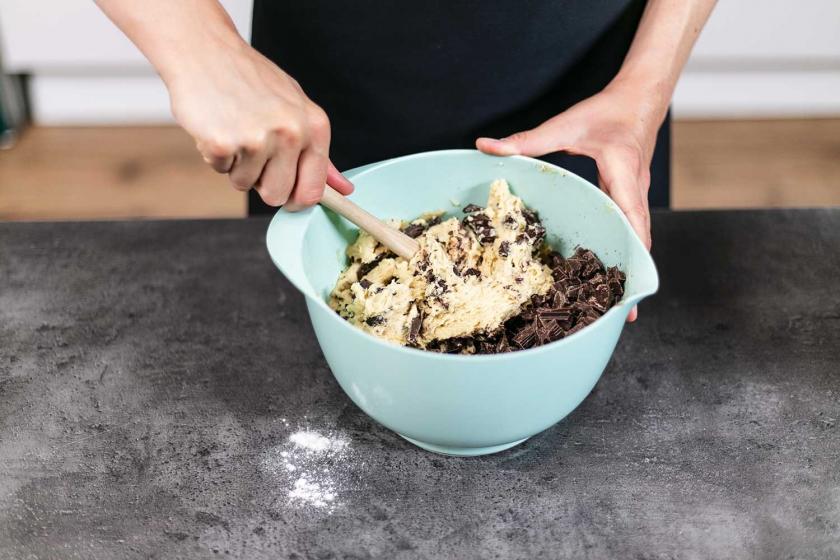 Schokolade wird unter den Teig für die American Cookies mit einem Holzlöffel gehoben.