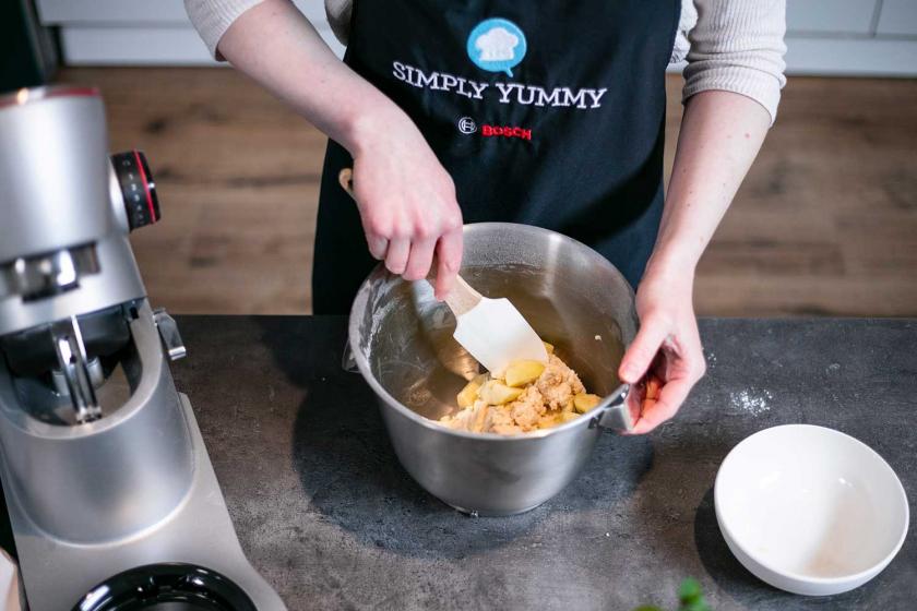 Äpfel werden mit einem Spatel unter den Teig für die Apfelballen vom Blech gehoben.