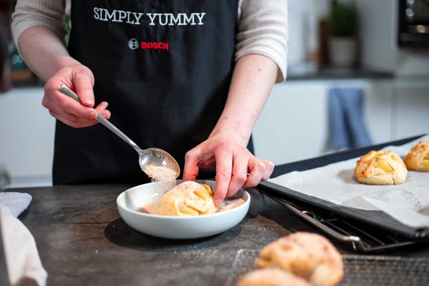 Die Apfelballen vom Blech werden in einer Schale mit Zimt-Zucker bestreut.