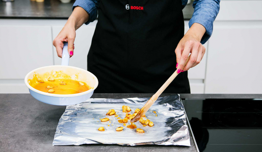 Die Karamellmandeln für den Apfelkuchen mit Quark werden aus der Pfanne auf ein Stück Alufolie gegeben.