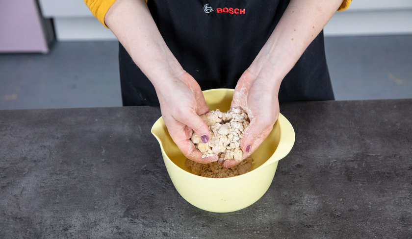 Der Streuselteig für den Aprikosenkuchen mit Streuseln wird mit den Händen zerkrümelt.