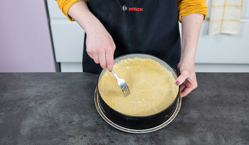 Der Boden für den Aprikosenkuchen mit Streuseln liegt in einer Springform und wird mit einer Gabel eingestochen.