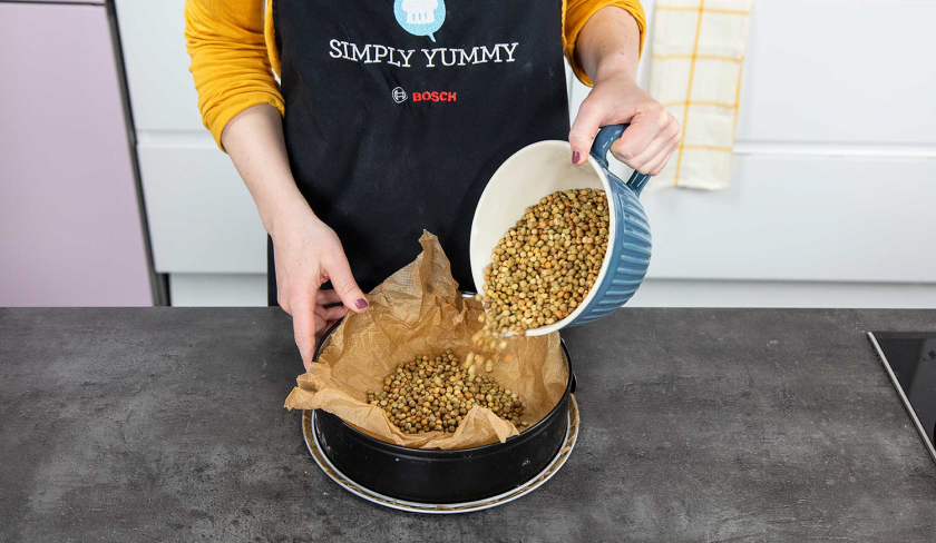 Backerbse werden in eine Springform mit Backpapier gegeben zum Vorbacken des Aprikosenkuchen mit Streuseln.