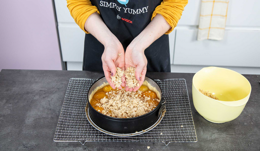 Jemand bedeckt den Aprikosenkuchen mit Streuseln.