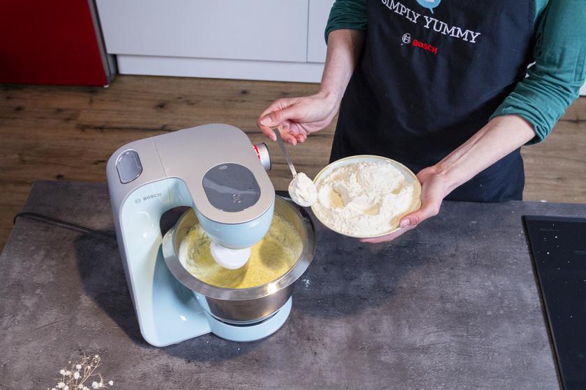 Mehl wird portionsweise zu flüssigen Zutaten in der Rührschüssel einer Küchenmaschine zugegeben.