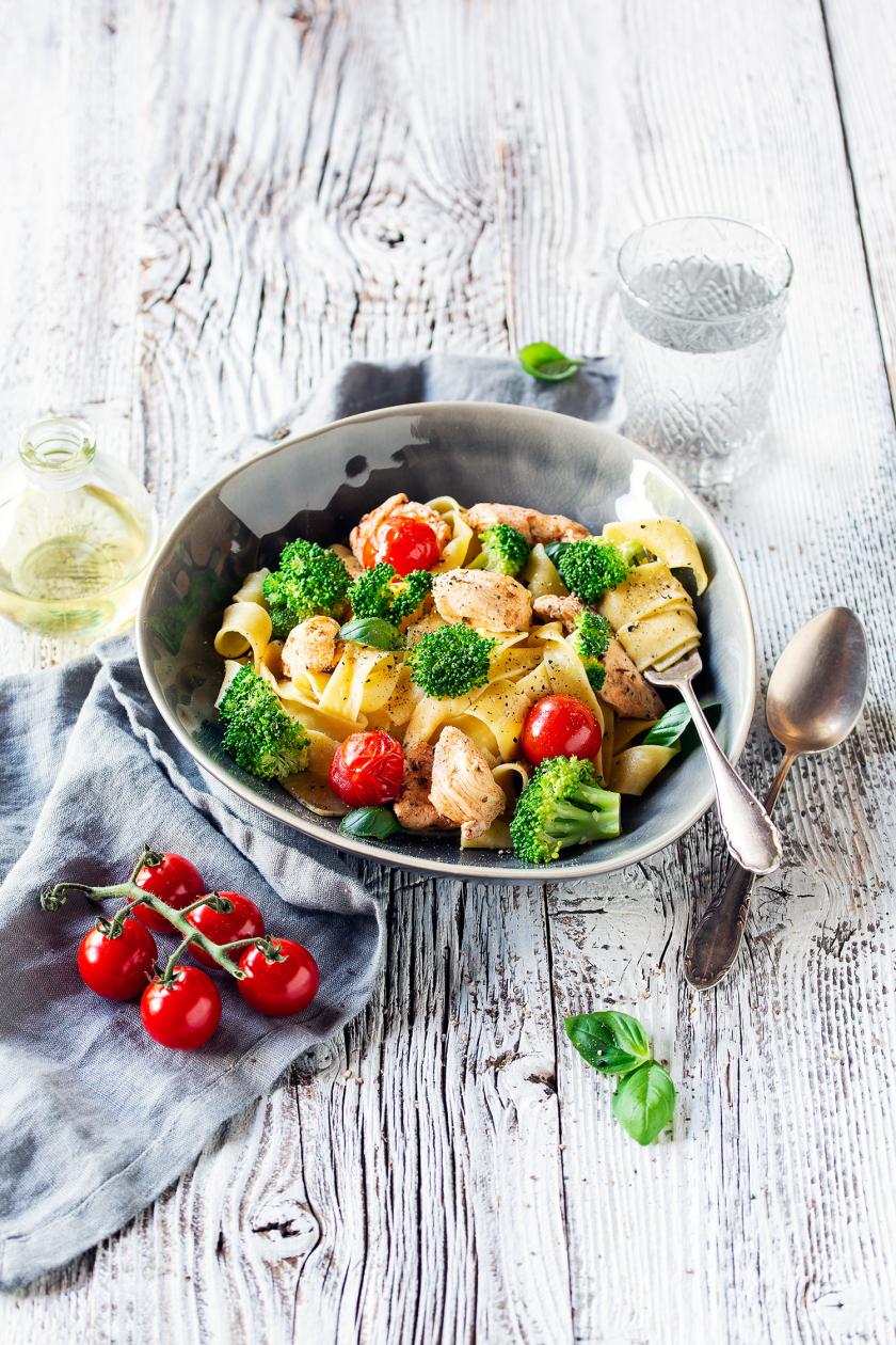Bandnudeln mit würzigem Hähnchen, Brokkoli und Tomaten in einem Teller angerichtet.