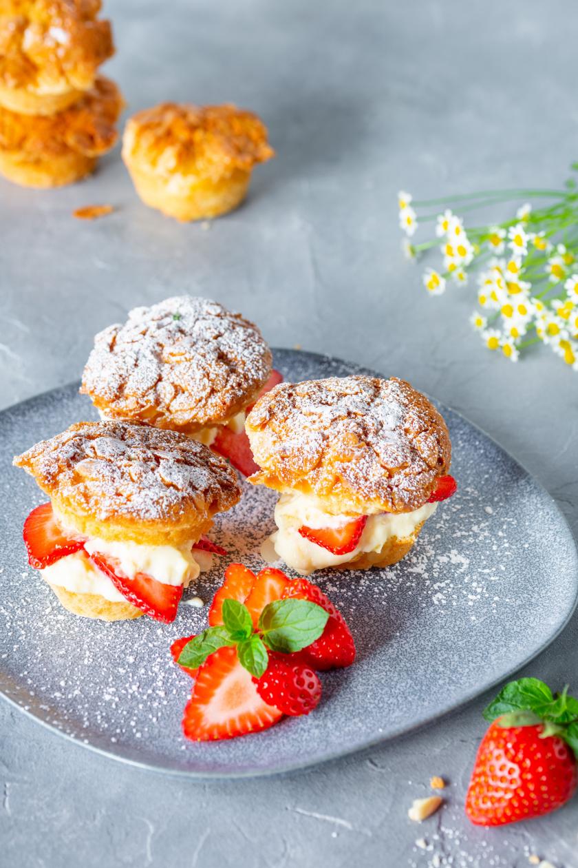 Mehrere Bienenstich Muffins mit Erdbeeren und Puderzucker auf einem Teller.