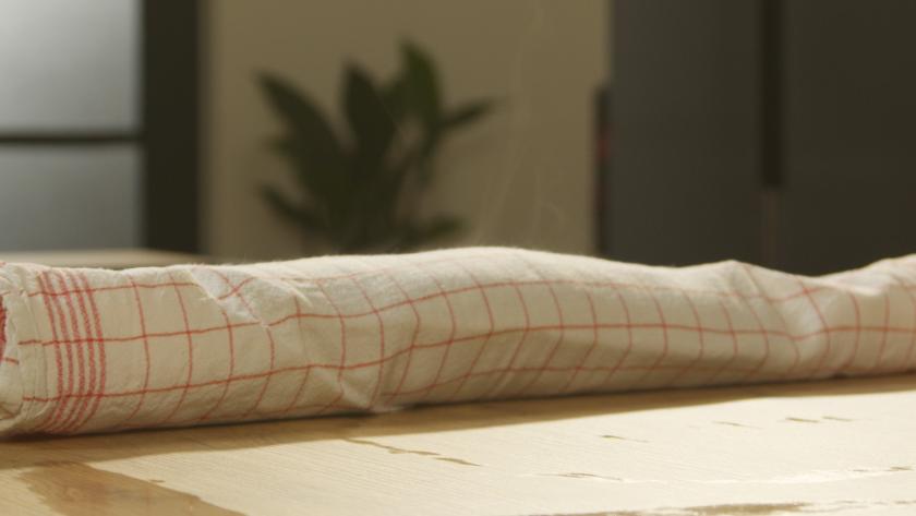 Biskuitrolle Schoko-Banane in einem Küchentuch aufgerollt.