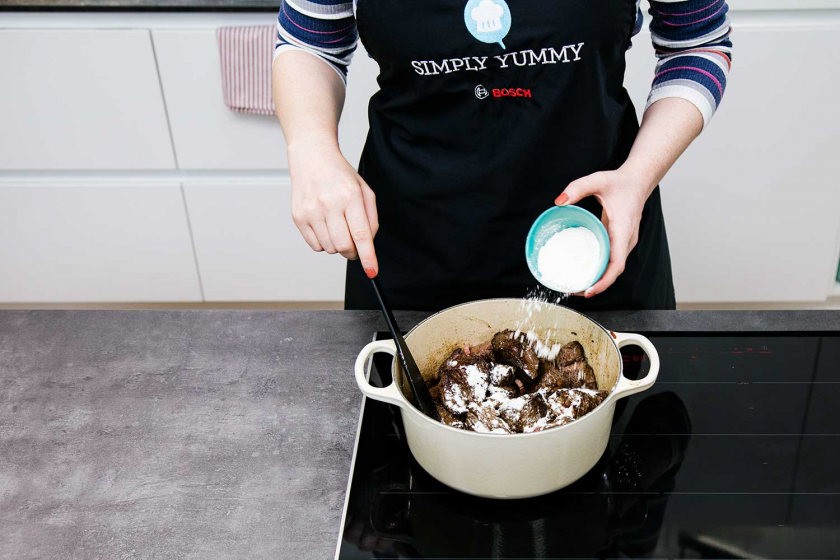 Mehl wird zum Fleisch für Boeuf Bourguignon in den Bräter gegeben.