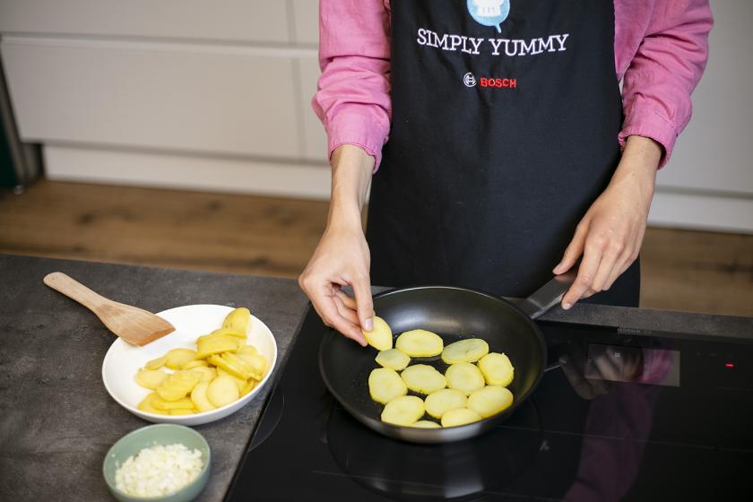 Kartoffelscheiben werden in eine Pfanne gegeben.