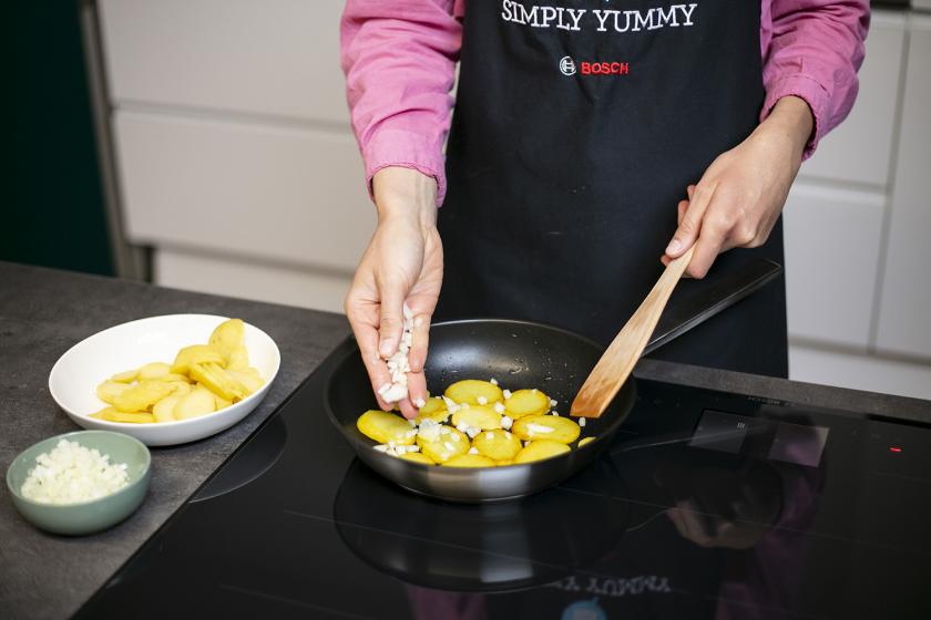 Zwiebeln werden zu den Bratkartoffeln aus gekochten Kartoffeln in die Pfanne gegeben.