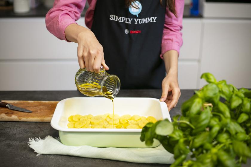 Kartoffelscheiben liegen in einer Auflaufform und werden mit Öl übergossen.