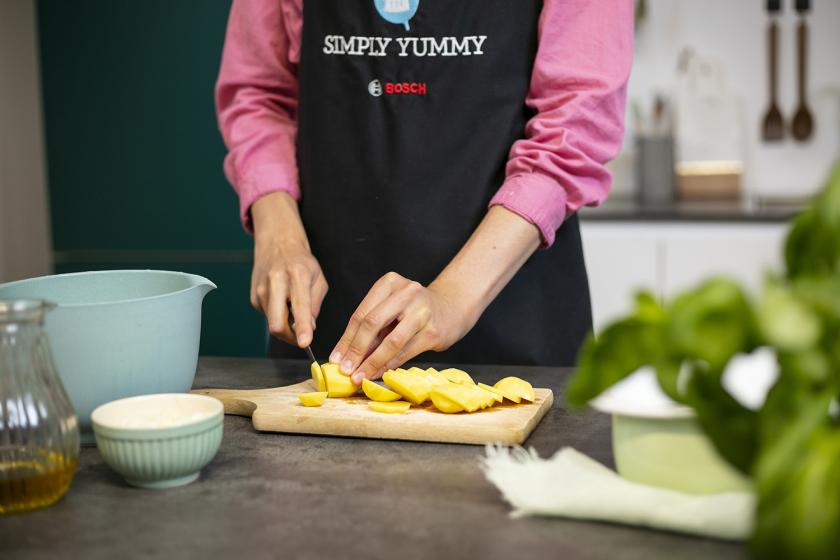 Kartoffeln werden auf einem Holzbrett in Scheiben geschnitten.
