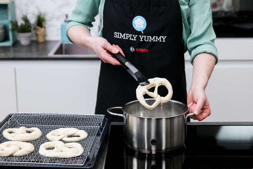 Die Brezel wird mit einer Zange aus dem Topf mit Lauge genommen.