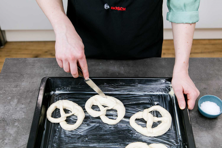 Die Brezel wird auf ein Backblech gelegt, auf dem bereits andere Brezel liegen.