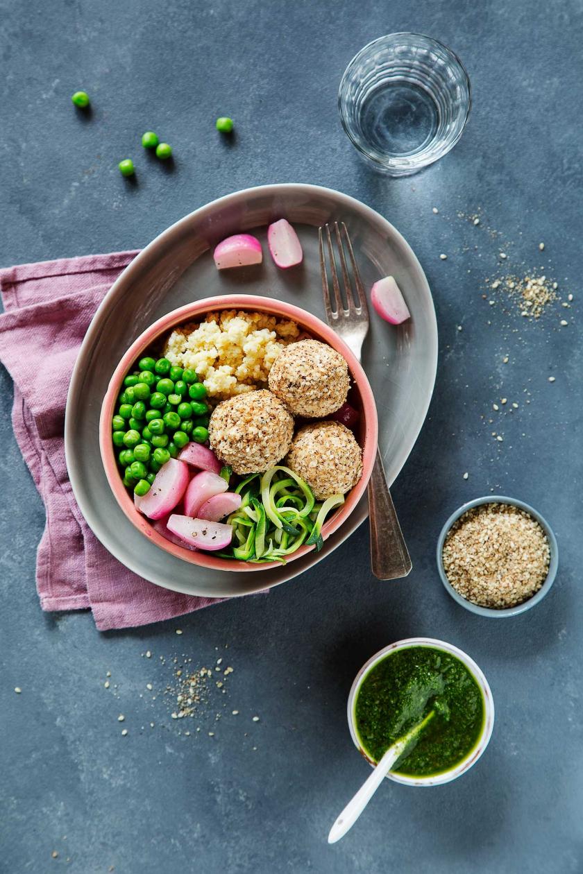 Buddha Bowl mit Frischkäsebällchen und Radieschen ist in einer Schüssel angerichtet und steht auf einem gedeckten Tisch.