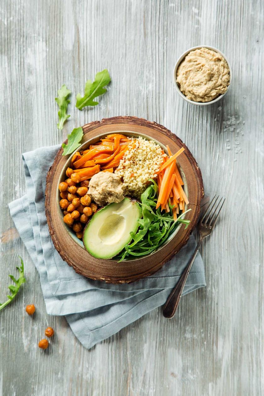 Buddha Bowl mit Süßkartoffeln und Kichererbsen ist in einer Schüssel angerichtet und steht auf einem Tuch.