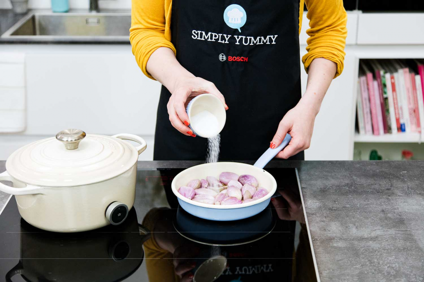 Für das Coq au Vin werden Zwiebeln in einer Pfanne gebraten und mit Zucker bestreut.