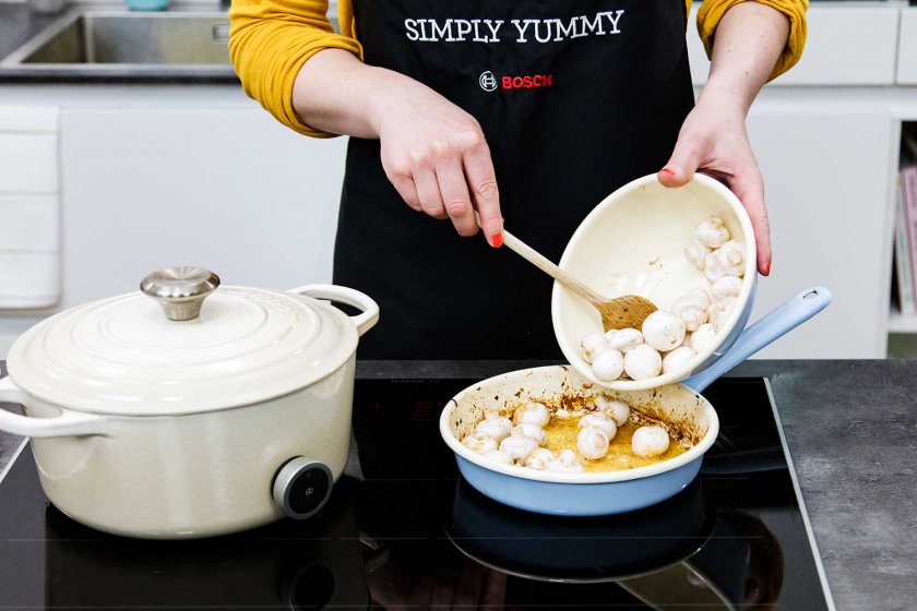 Für das Coq au Vin werden Pilze in eine Pfanne gegeben und geschmort.