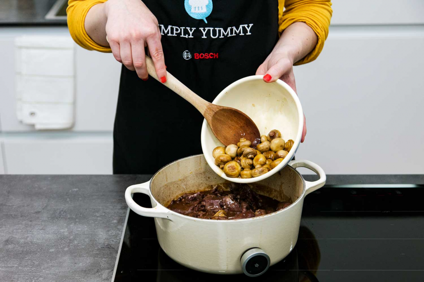 Schmorpilze werden in den Topf zum Coq au Vin gegeben.