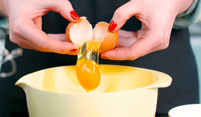 Ein Ei für den Teig für die Crème Brulée Brownie Törtchen wird in eine Schüssel gegeben.