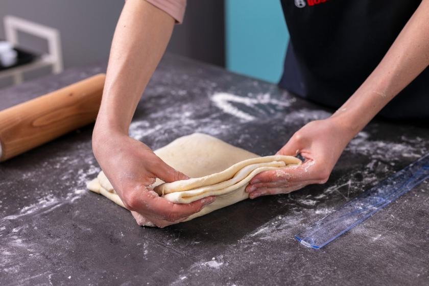 Tourierter Croissant Teig wird in den Händen gehalten.