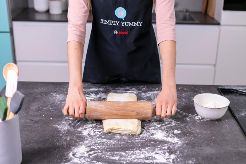 Croissant Teig wird auf einer bemehlten Arbeitsfläche ausgerollt.