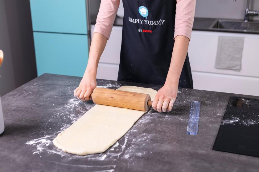Croisssant Teig wird mit einem Nudelholz ausgerollt.