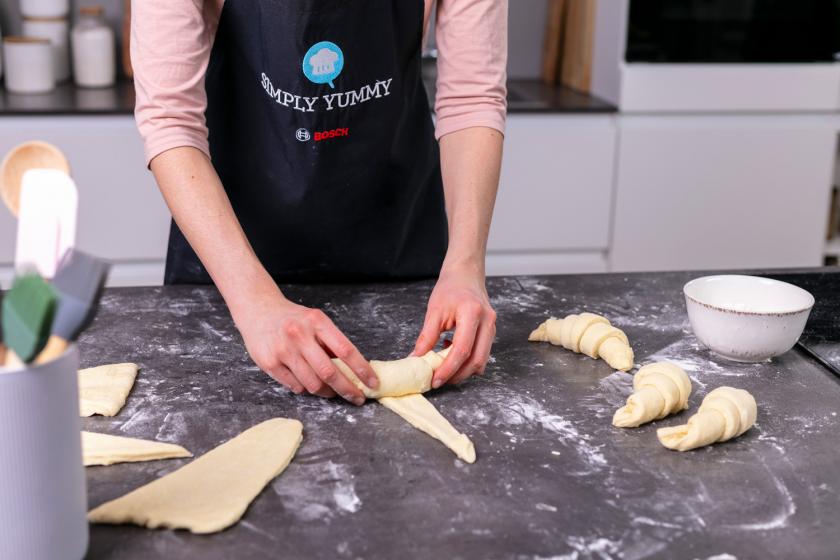 Teig wird zu Croissants aufgerollt.
