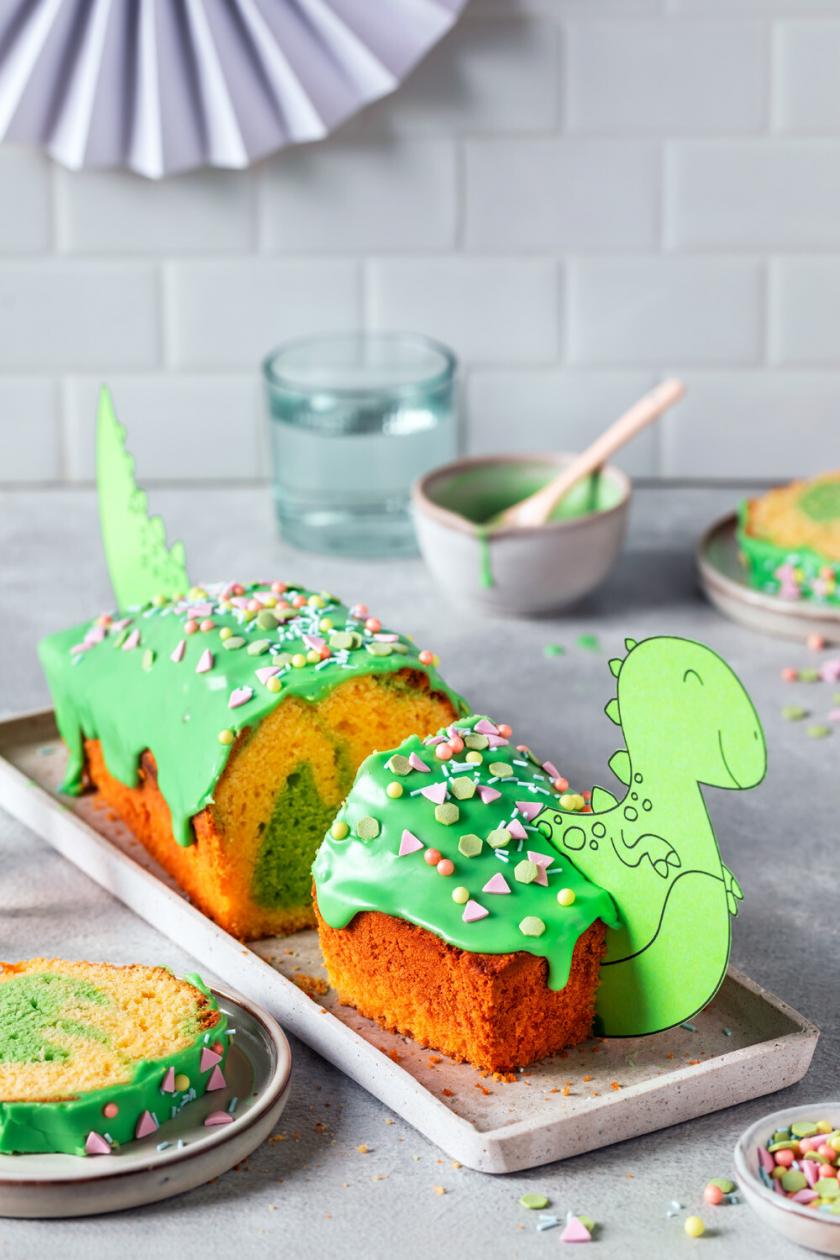 Grüner Dino Kuchen dekoriert mit Schablone und Streuseln angeschnitten auf einer Kuchenplatte