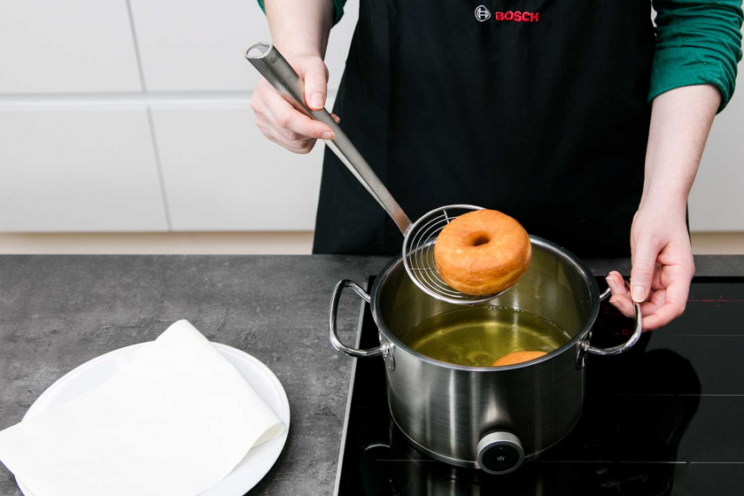 Donuts werden mit einer Schaumkelle aus einem Topf gehoben.